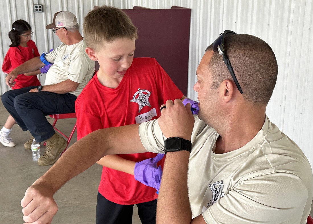 Claypool Town Marshal Ben Sanders (R) has a tourniquet put on his arm by Camp HERO camper Brayden Wednesday during a “Stop the Bleed” race to see which campers could put a tourniquet on the fastest. Photo by David Slone, Times-Union.