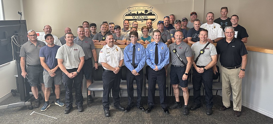 Tristan Pass and Logan Keener (C, blue shirts) took the oath of office Friday as Warsaw-Wayne Fire Territory firefighters. They are surrounded by Fire Chief Brian Mayo (to the left of Pass and Keener), Mayor Joe Thallemer (R, front row) and the other members of the fire department. Photo by David Slone, Times-Union