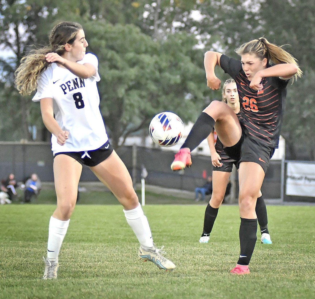 Warsaw senior Kaiden Pepper uses some body English to kick the ball over Penn's Emily Keegan during the first half of Thursday night's home game. Photo by Gary Nieter.