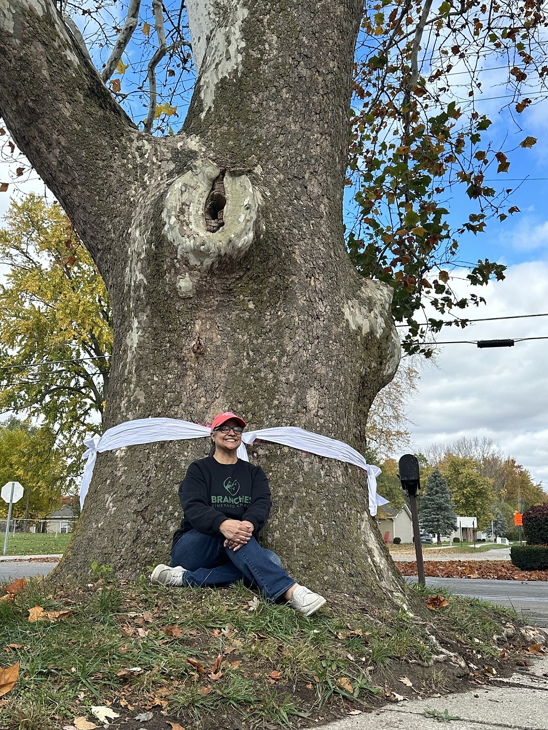 Gita Kamdar sits next to the centuries-old Sycamore tree in her yard at 1702 E. Sheridan St., Warsaw, during Saturday’s rally to save the tree. Photo by David Slone, Times-Union