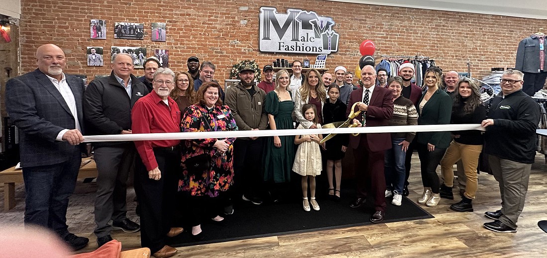 Male Fashions owner Tim Hamann (center, with scissors) cuts the ribbon for the ribbon-cutting ceremony Friday with the Kosciusko Chamber of Commerce for the men’s clothing store’s new location at 122 S. Buffalo St., Warsaw. He is surrounded by family, friends, Chamber staff and ambassadors. Photo by David Slone, Times-Union