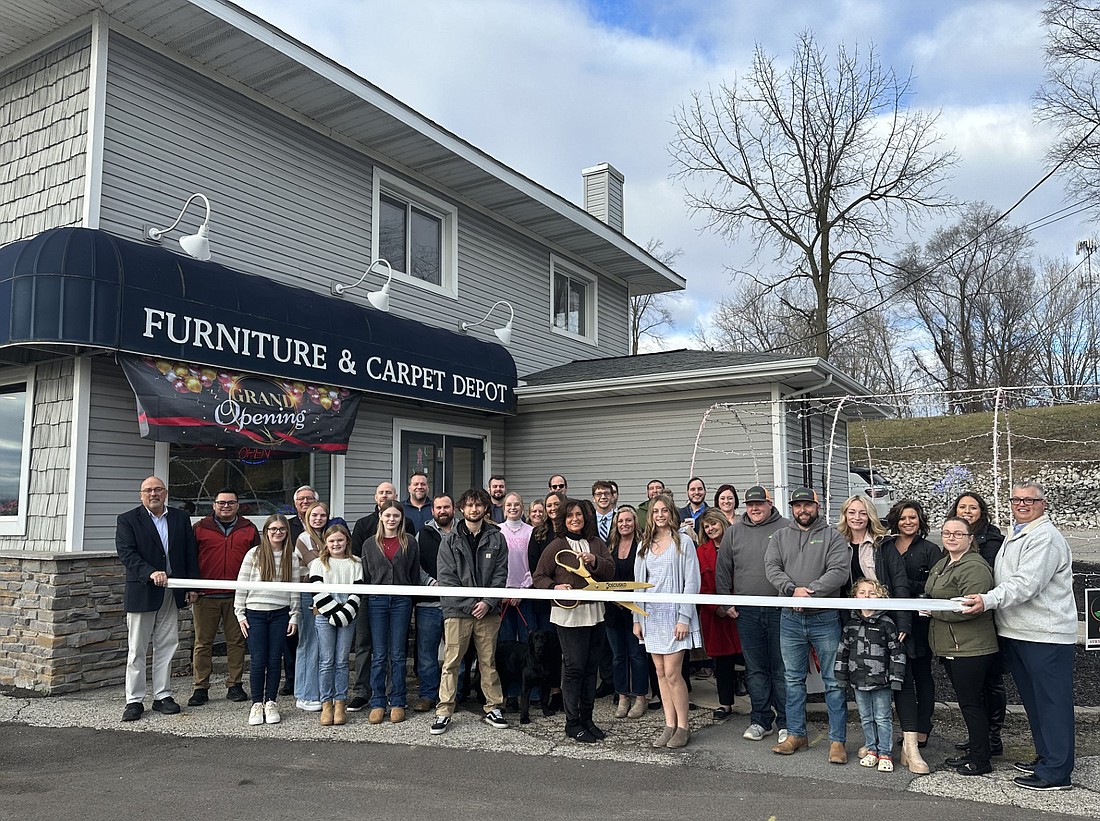 Judy Ness (C, with scissors), owner of Carpet Depot Interiors, 25 Kings Hwy., Winona Lake, cuts the ribbon Thursday during a ribbon-cutting ceremony with the Kosciusko Chamber of Commerce for Winona Live. She is surrounded by Chamber staff and ambassadors, as well as employees and owners of the other businesses that are located within the building. Photo by David Slone, Times-Union