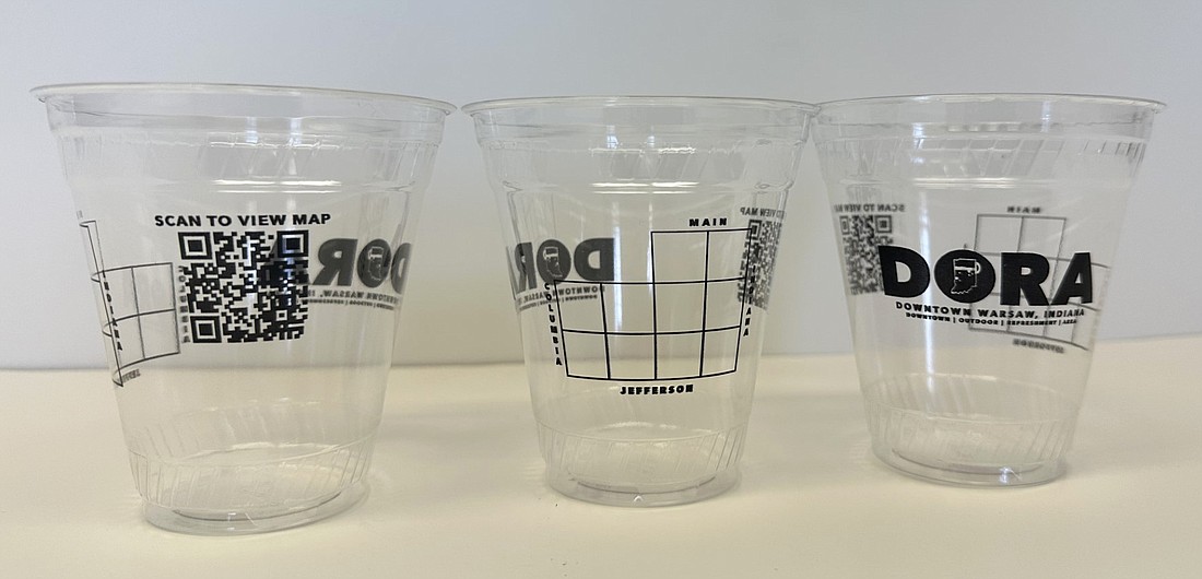 Shown are the Designated Outdoor Refreshment Area (DORA) cups purchased by Main Street Warsaw for use by the establishments that have been approved to be a part of the DORA. On them are (L to R) a QR Code to view a map of the DORA, a map of the DORA and DORA wording. Photo by David Slone, Times-Union