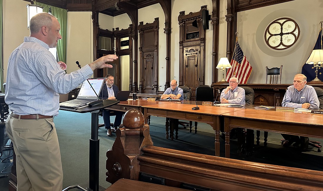 Rusty Holt (L, standing), supervising traffic engineer at WSP, the engineering company studying U.S. 30 East for the Indiana Department of Transportation, gives the Kosciusko County Commissioners an update Monday on the study. Pictured (seated, L to R) are county attorney Ed Ormsby and Commissioners Cary Groninger, Bob Conley and Brad Jackson. Photo by David Slone, Times-Union