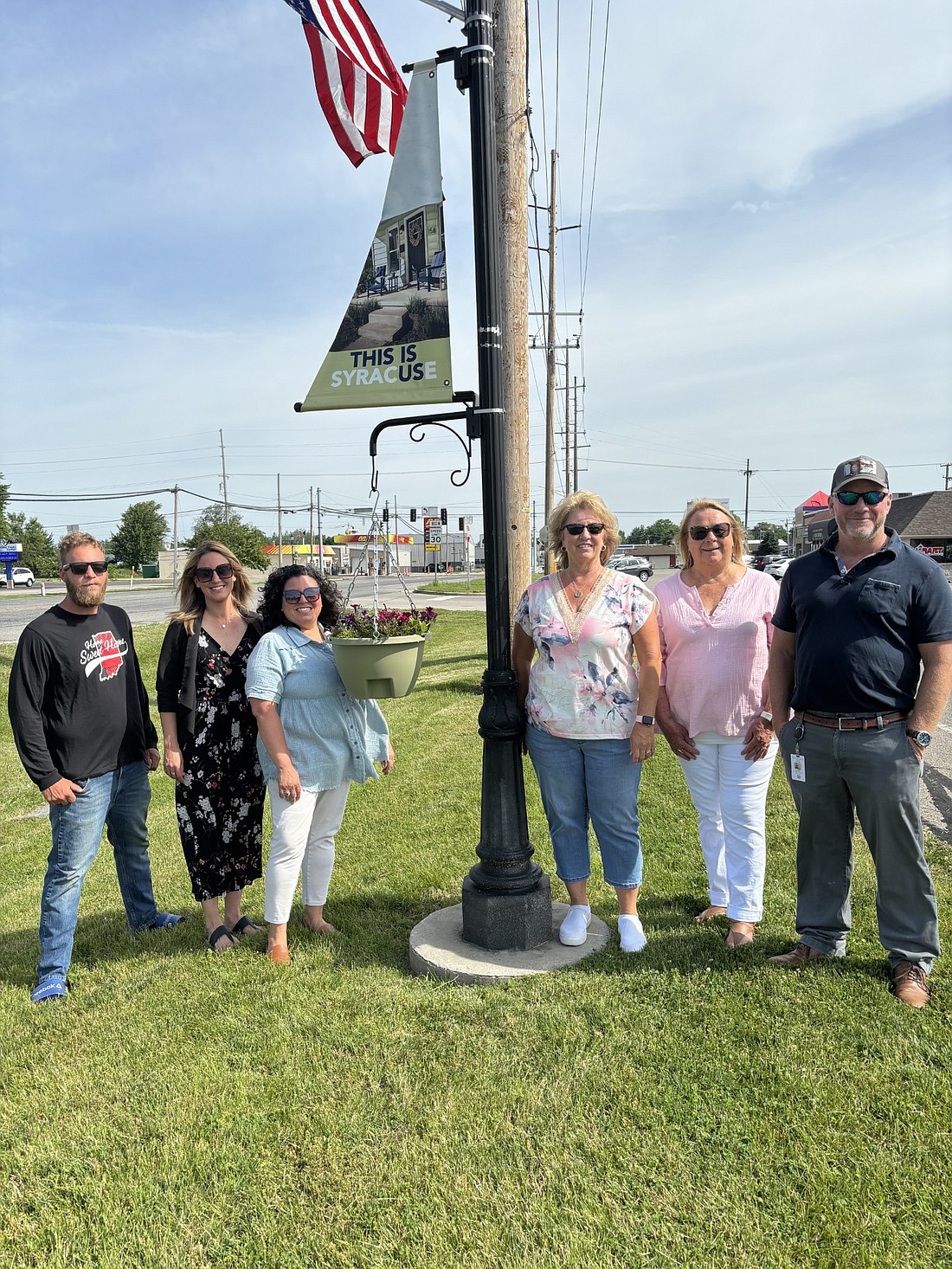 Members of the Syracuse Beautification Committee met Tuesday morning to unveil the new flower pot planters and banner signs they recently placed in the Wawasee Village area. Pictured (L to R) are Will Bennett, Ashley Dillon, Virginia Cazier, Michelle Owens, Cindy Kaiser and David Wilkinson. Members not available for photo include Kip Schumm and Chad Jonsson. Photo by Denise Fedorow.