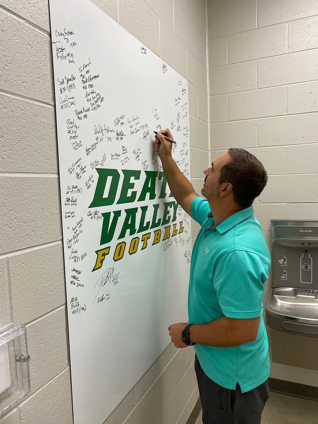 Tippecanoe Valley School Board member Aaron Zolman puts his name to a sign in one of the new Valley locker rooms, which bears the names of Valley football players. Photo by Leah Sander, InkFreeNews