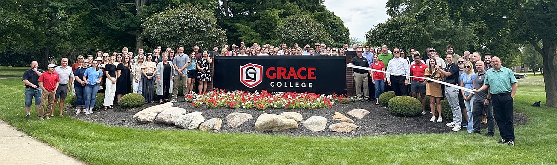 Surrounded by Grace students and staff, along with Kosciusko Chamber of Commerce staff and ambassadors, Grace President Dr. Drew Flamm (right, with scissors) cuts the ribbon Monday for the rebranding of Grace College and Grace Theological Seminary. Photo by David Slone, Times-Union.