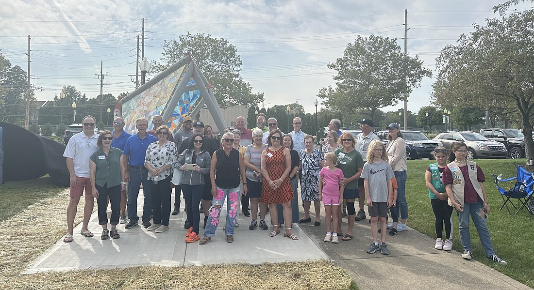 The tarp on the newest sculpture in Warsaw, “Reflection,” was taken off while everyone’s back was turned toward it so they could turn in unison to see it for the first time Friday. Photo by David Slone, Times-Union