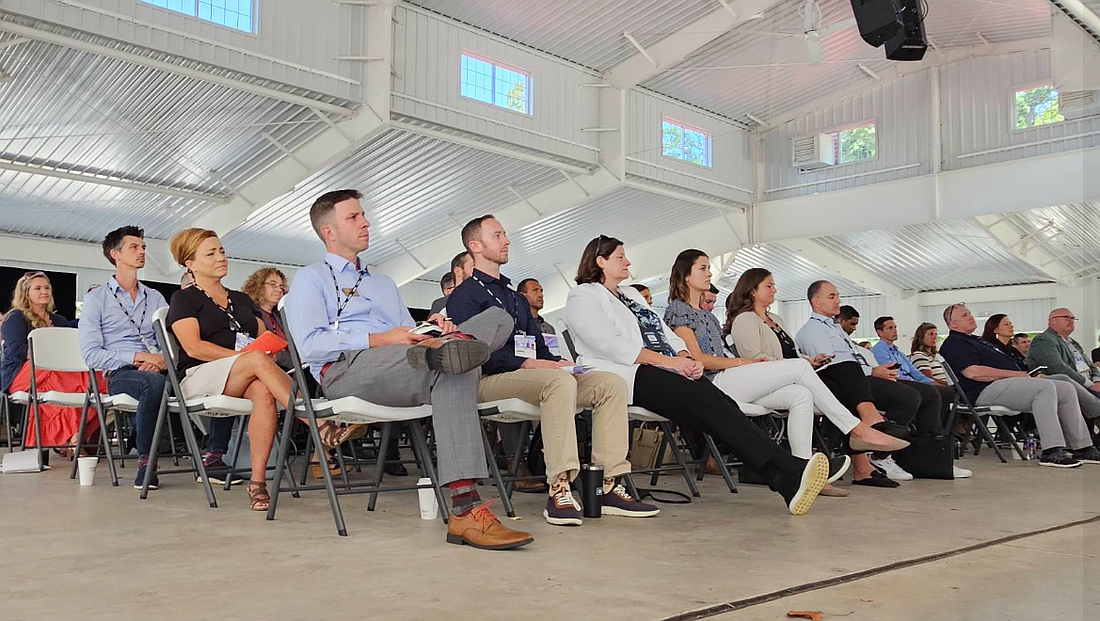 Grace College President Drew Flamm (front row with his legs crossed) listens to a presentation during the Plug and Play expo in Winona Lake on Tuesday