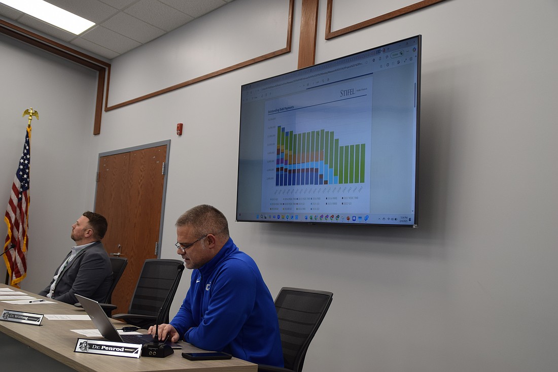 Dr. Brandon Penrod (R), finance officer for Wawasee Community Schools, explains the slide behind him, which shows the corporation's outstanding debt payments during a public hearing Tuesday night on a proposed student activity center and deferred maintenance projects. Dr. Stephen Troyer (L), superintendent of schools, looks at the slide on another screen. Photo by Lauren Zeugner, InkFreeNews